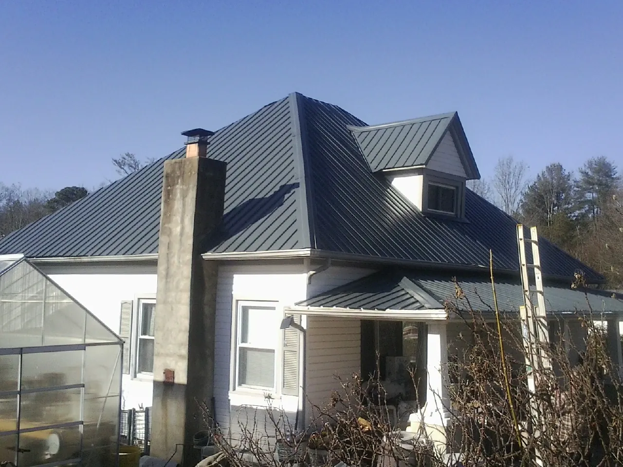 Dark blue standing seam metal roof on a white farmhouse with dormer — Slate & Tile Roof Repair by Roofing Brothers in Gerlaw