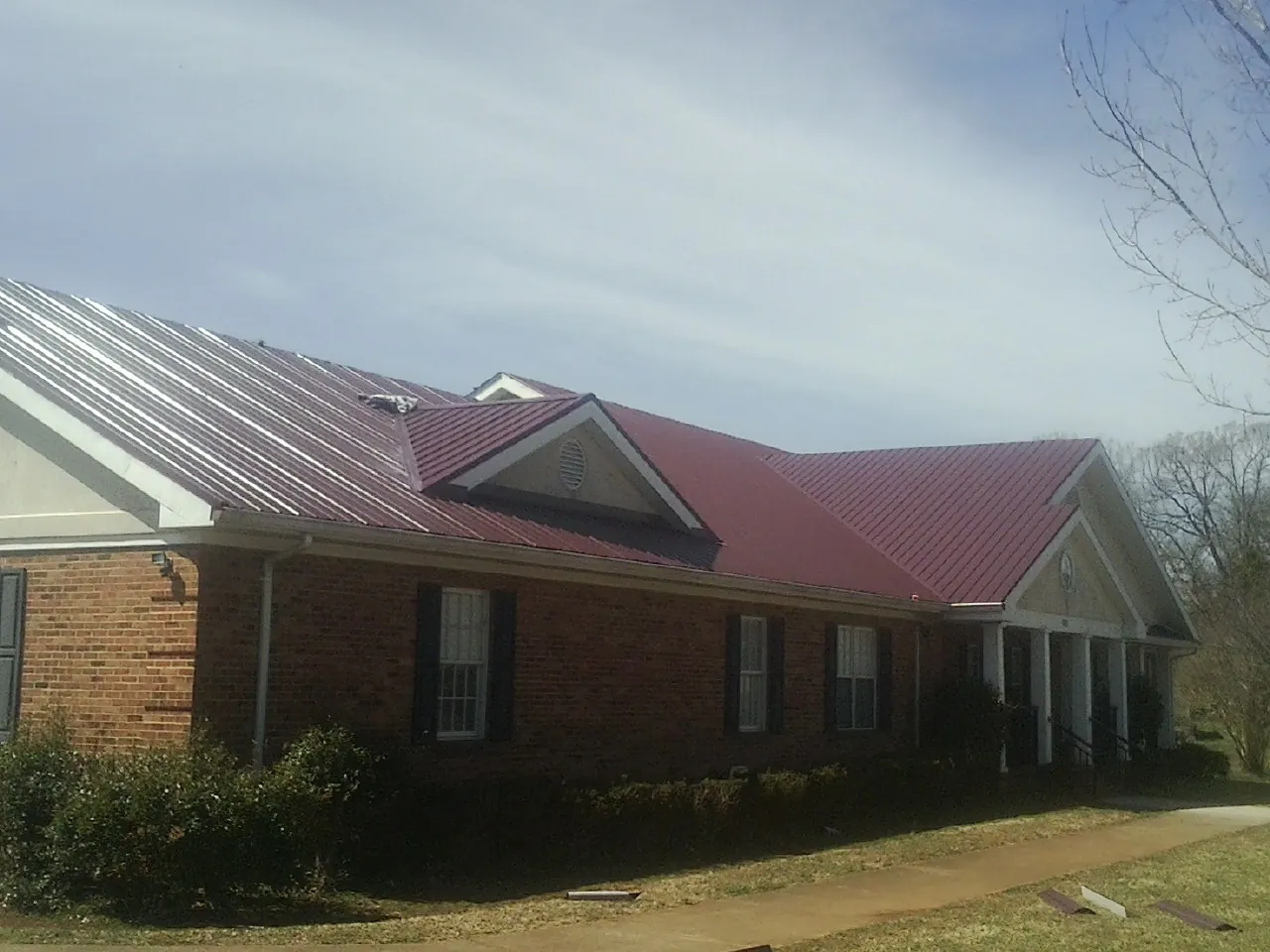 Red metal roof with gabled entries on a long brick building, from a Hail Damage Roof Repair job in Gerlaw