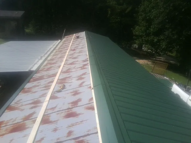 Old rusted panels beside newly installed green metal roofing — Wind Damage Roof Repair by Roofing Brothers in Gerlaw