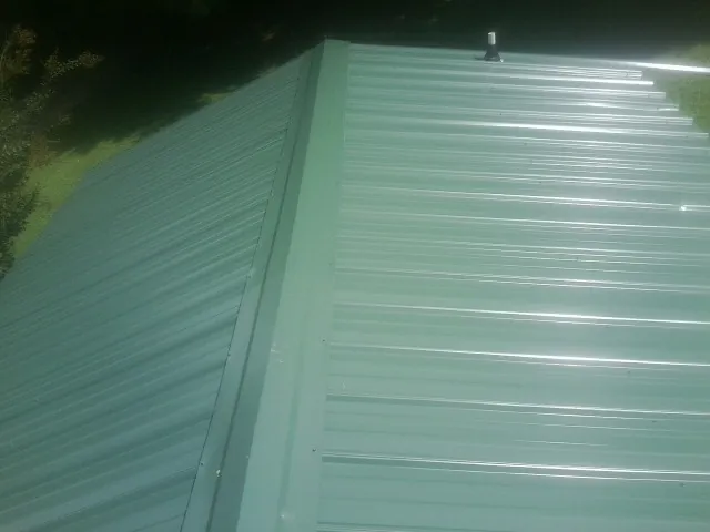 New green metal panels meeting at the ridge of a roof — Flat Roof Repair work by our crew in Gerlaw