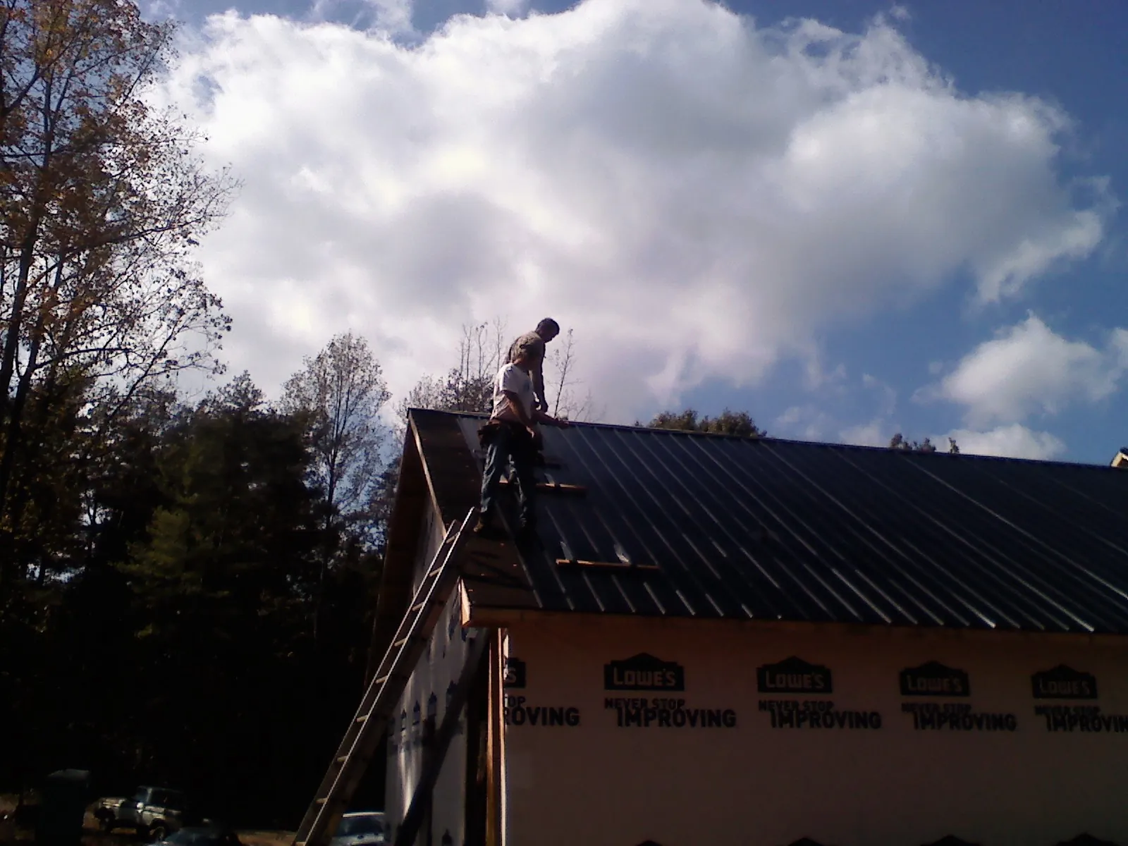 Roofer fastening dark metal panels high against a cloudy sky, from a Roof Inspection job in Gerlaw