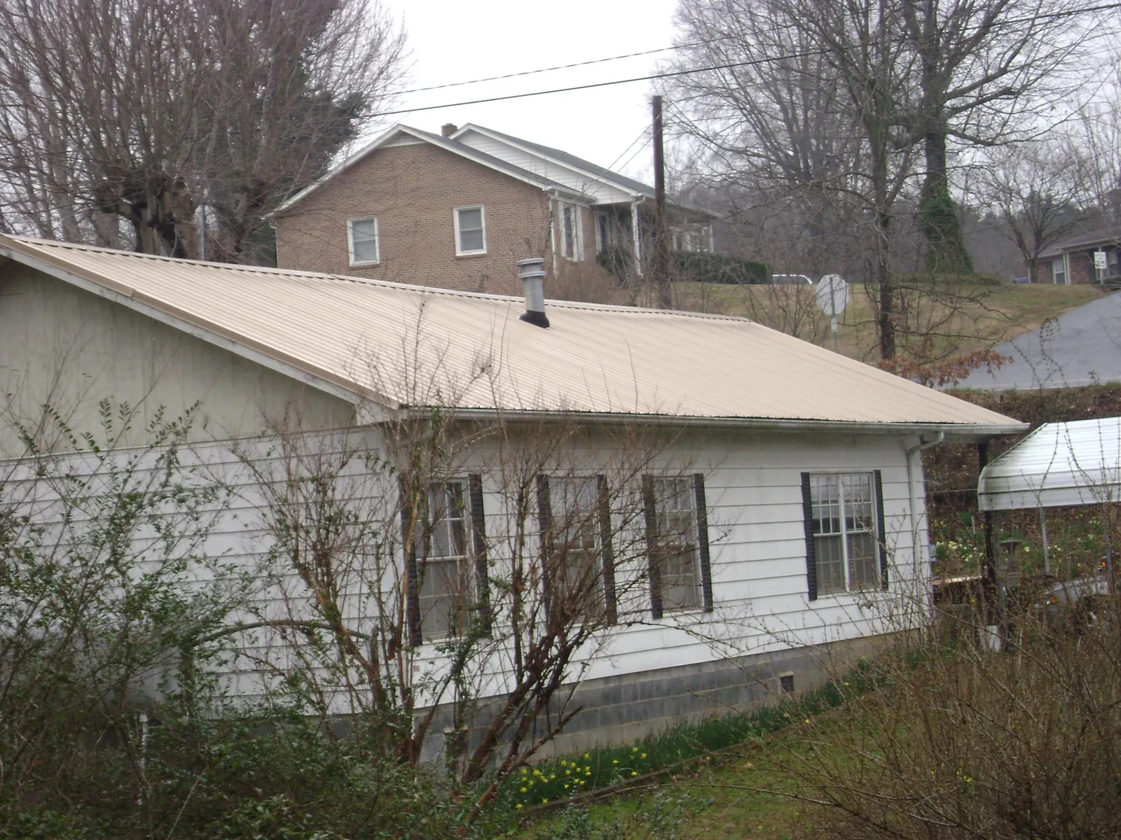 Tan metal roof on a white sided house set into a hillside — Commercial Roofing by Roofing Brothers in Gerlaw